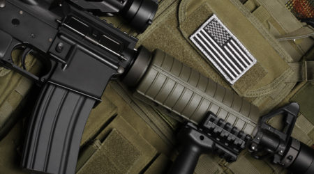 Military concept, still life. Tactical vest with U.S. battle flag and assault rifle with red-dot sight and tactical grip close-up. Studio shot.